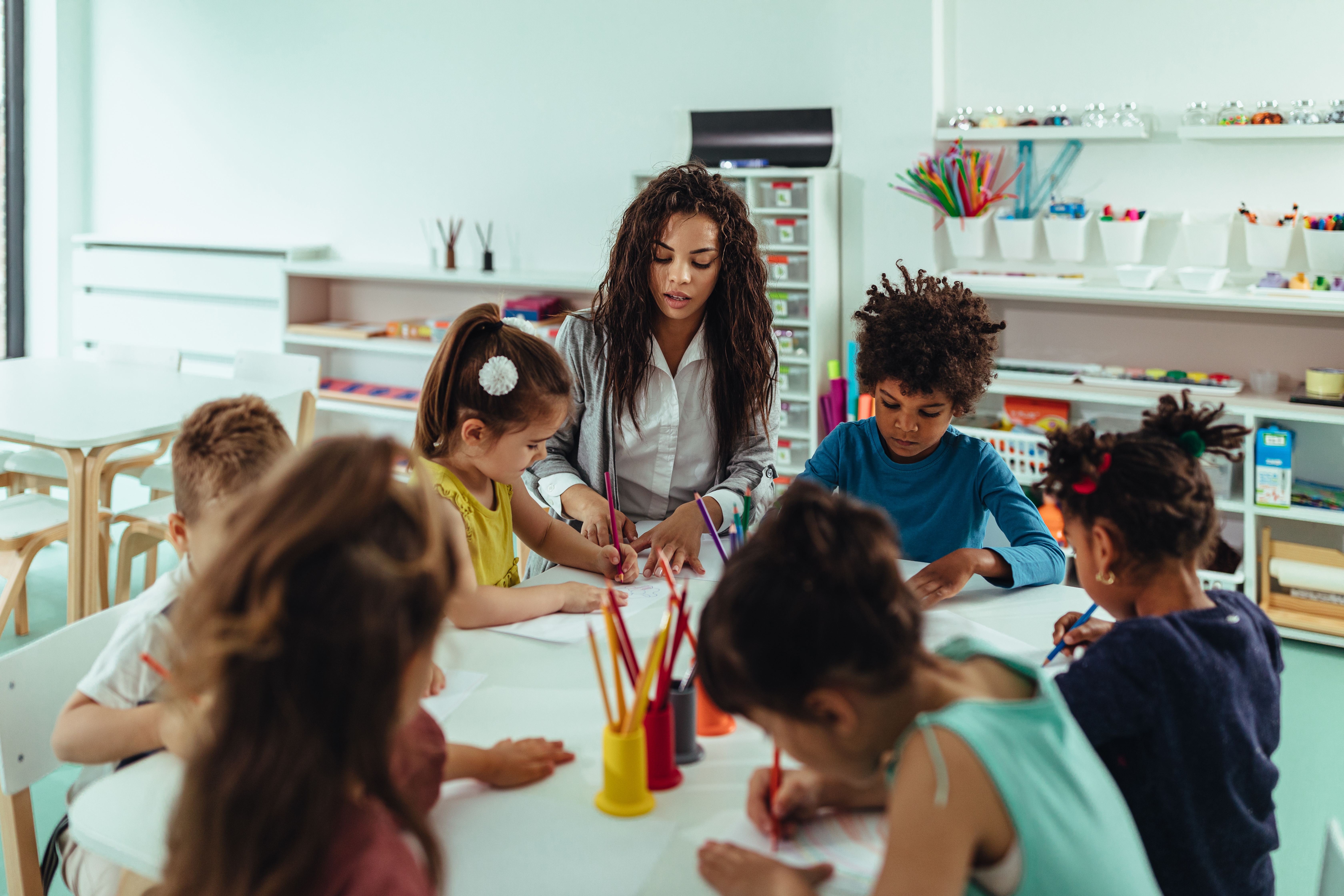 Early Childhood Education and Care (ECEC) teacher and students colouring at a table in a classroom