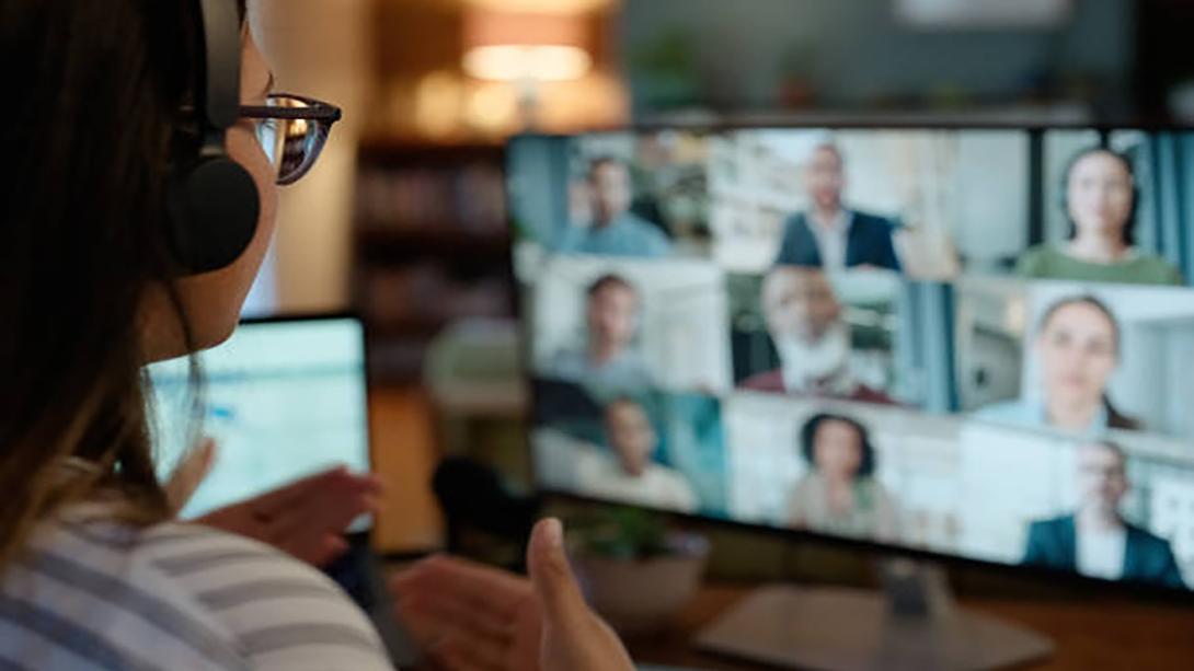 Back of woman engaging with group of people visible on laptop screen