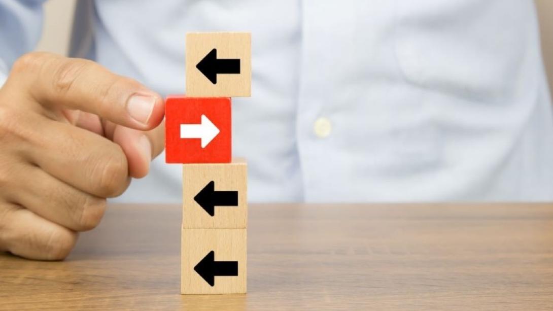 Four small building blocks with arrows on them piled on top of each other with one red block pointing in an opposite direction then the rest