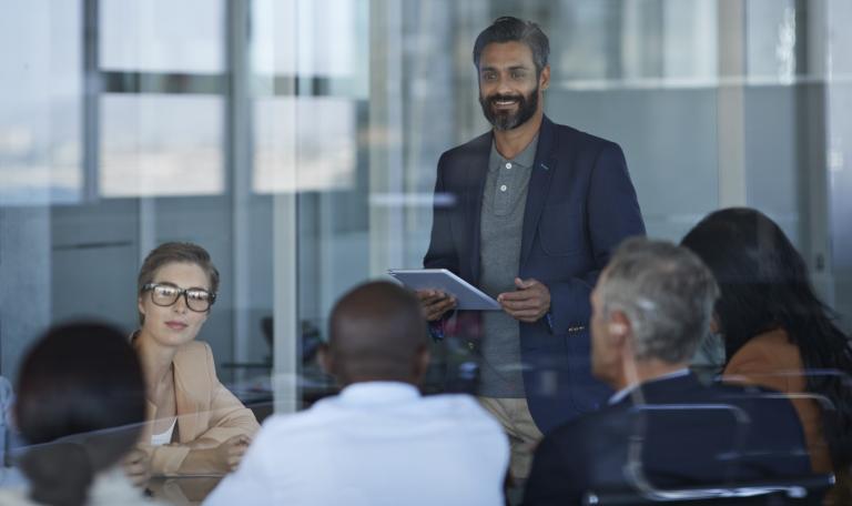 A man stands while listening to a small group of people in an office environment
