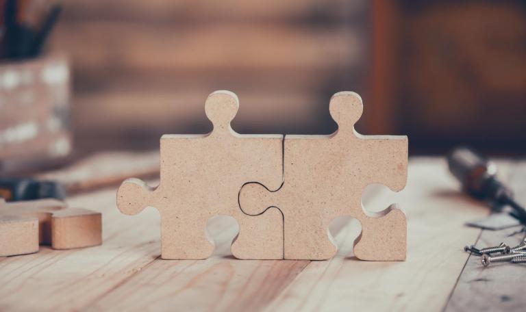 Two puzzle pieces joined together sitting on a woodworking table