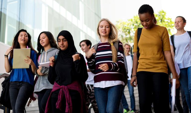 Group of students with backpacks smiling, talking and walking with books