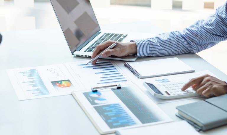 Finance worker sitting at desk using a calculator, looking at papers and using the computer