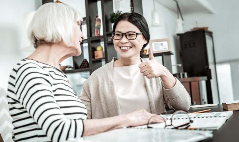 Support worker giving a thumbs up to elderly patient while they are sitting at a desk looking at documents
