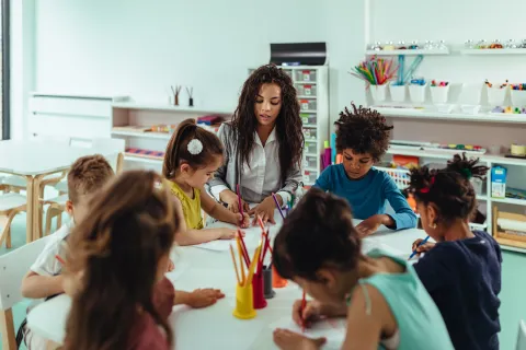 Early Childhood Education and Care (ECEC) teacher and students colouring at a table in a classroom
