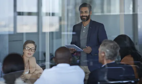 A man stands while listening to a small group of people in an office environment