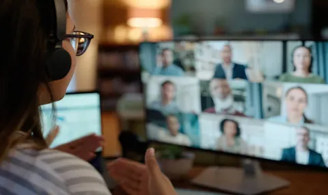 Back of woman engaging with group of people visible on laptop screen