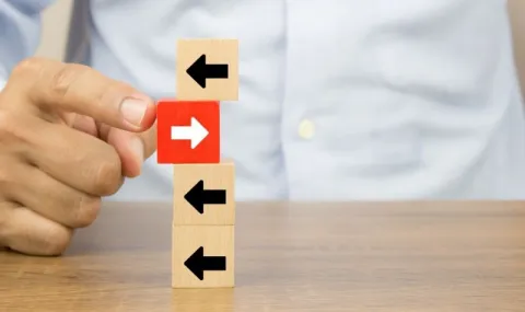 Four small building blocks with arrows on them piled on top of each other with one red block pointing in an opposite direction then the rest