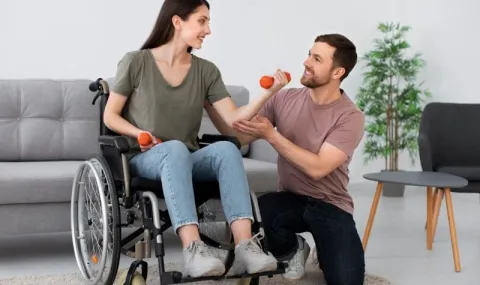 Male student in wheelchair talking to two fellow students at a desk looking at their laptops