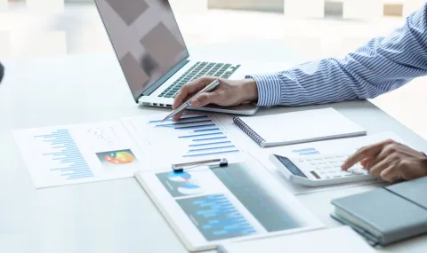 Finance worker sitting at desk using a calculator, looking at papers and using the computer