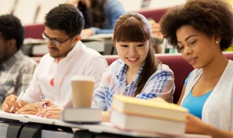 Female and male students sitting in a university lecture looking at books