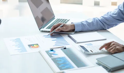Finance worker entering data into calculator while sitting at a desk in an office environment